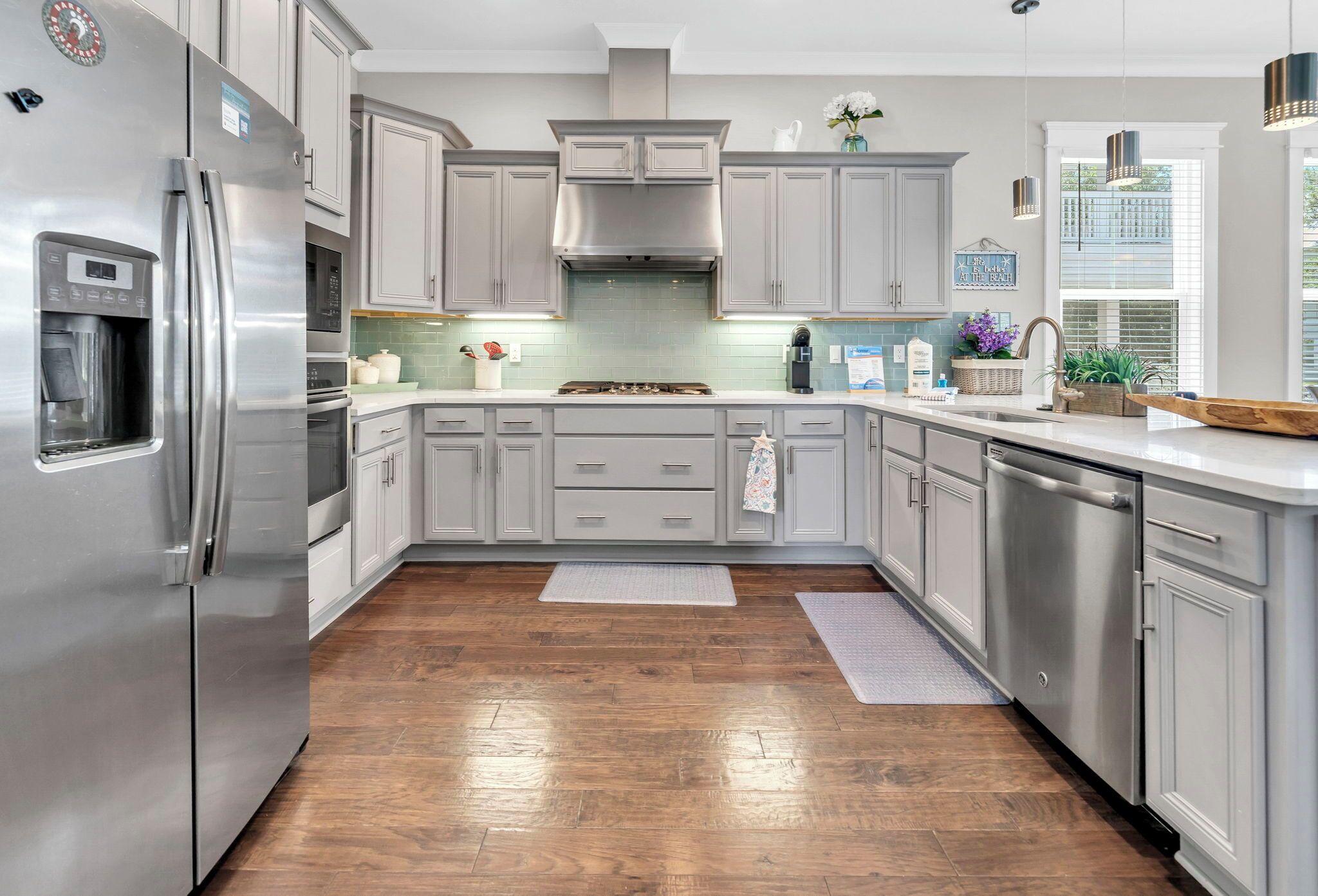 A modern kitchen with stainless steel appliances, grey cabinets, and a wooden floor.