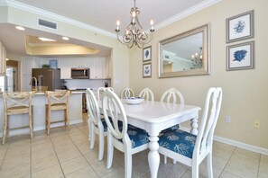 Uma área de refeições com mesa e cadeiras brancas, um candelabro e obras de arte emolduradas na parede.