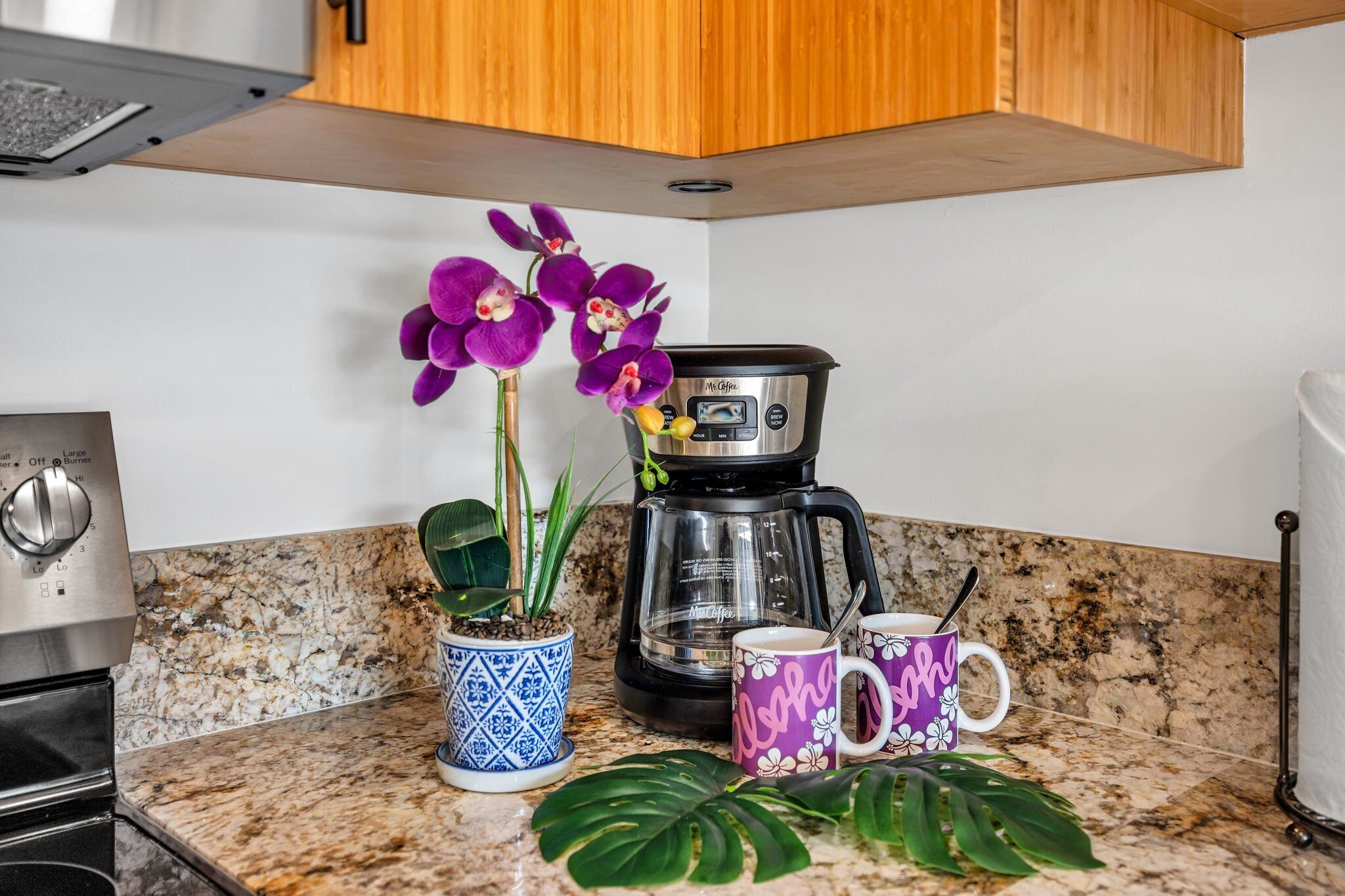 A kitchen with a coffee maker, two mugs, and a potted plant.