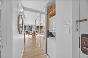 A modern kitchen with a built-in oven, a wooden shelf with a basket, and a view of the dining area through glass doors.