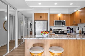 A modern kitchen with wooden cabinets, stainless steel appliances, a marble countertop, and a fruit bowl.