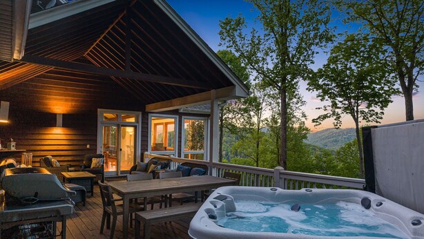 Une terrasse en bois avec coin salon extérieur, un jacuzzi et une vue sur les montagnes.