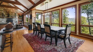 Un vaste espace dédié à la salle à manger, avec une grande table et des chaises, une cheminée en pierre et de grandes fenêtres offrant une vue sur l’extérieur.