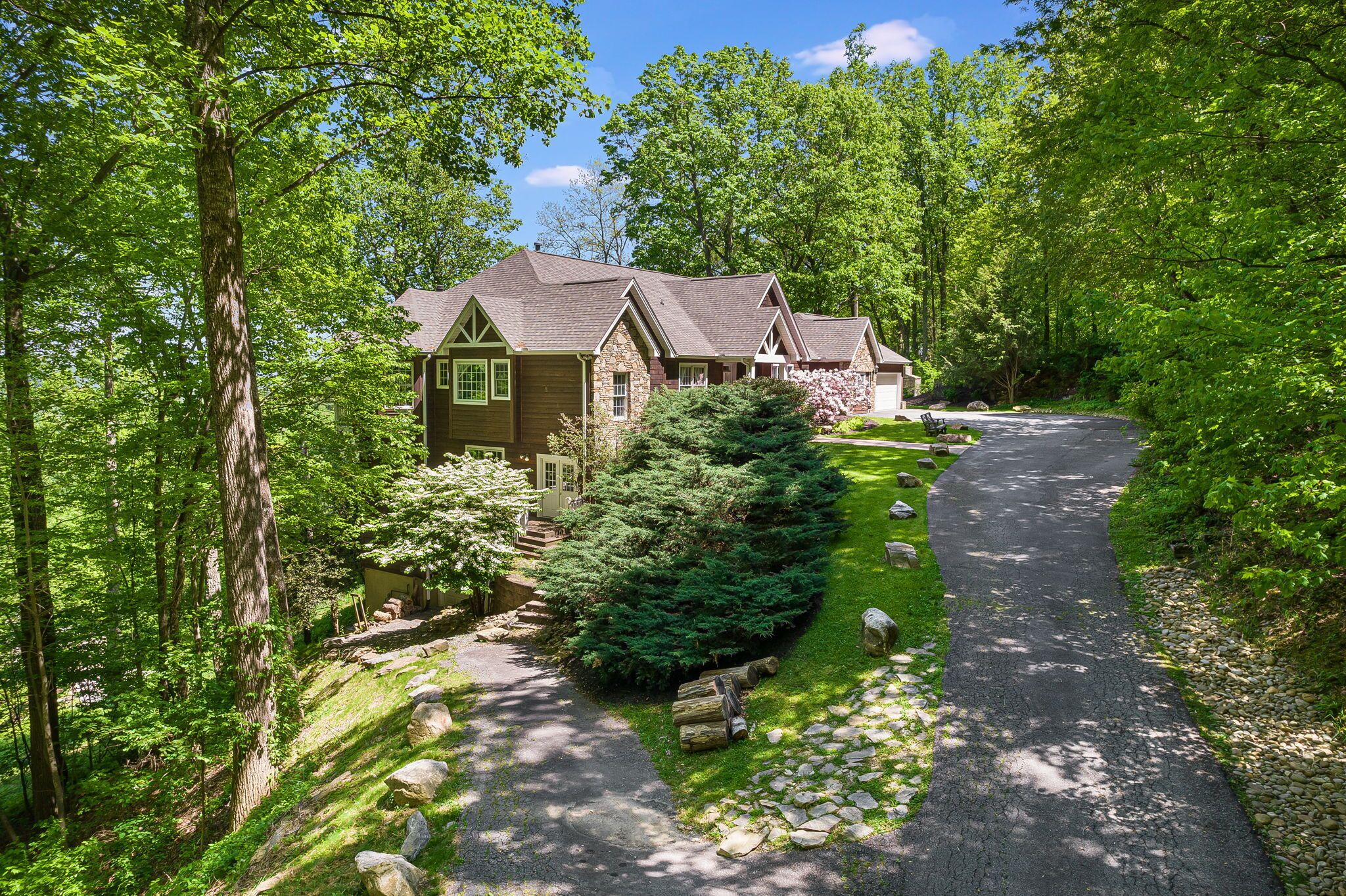 A two-story house with a stone facade, a covered porch, and a driveway leading to a gated entrance.