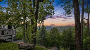Une cabane dotée d’une terrasse, entourée d’arbres et offrant une vue sur une vallée boisée.