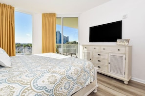 A bedroom with a large bed, a dresser, a television, and a balcony with a city view.