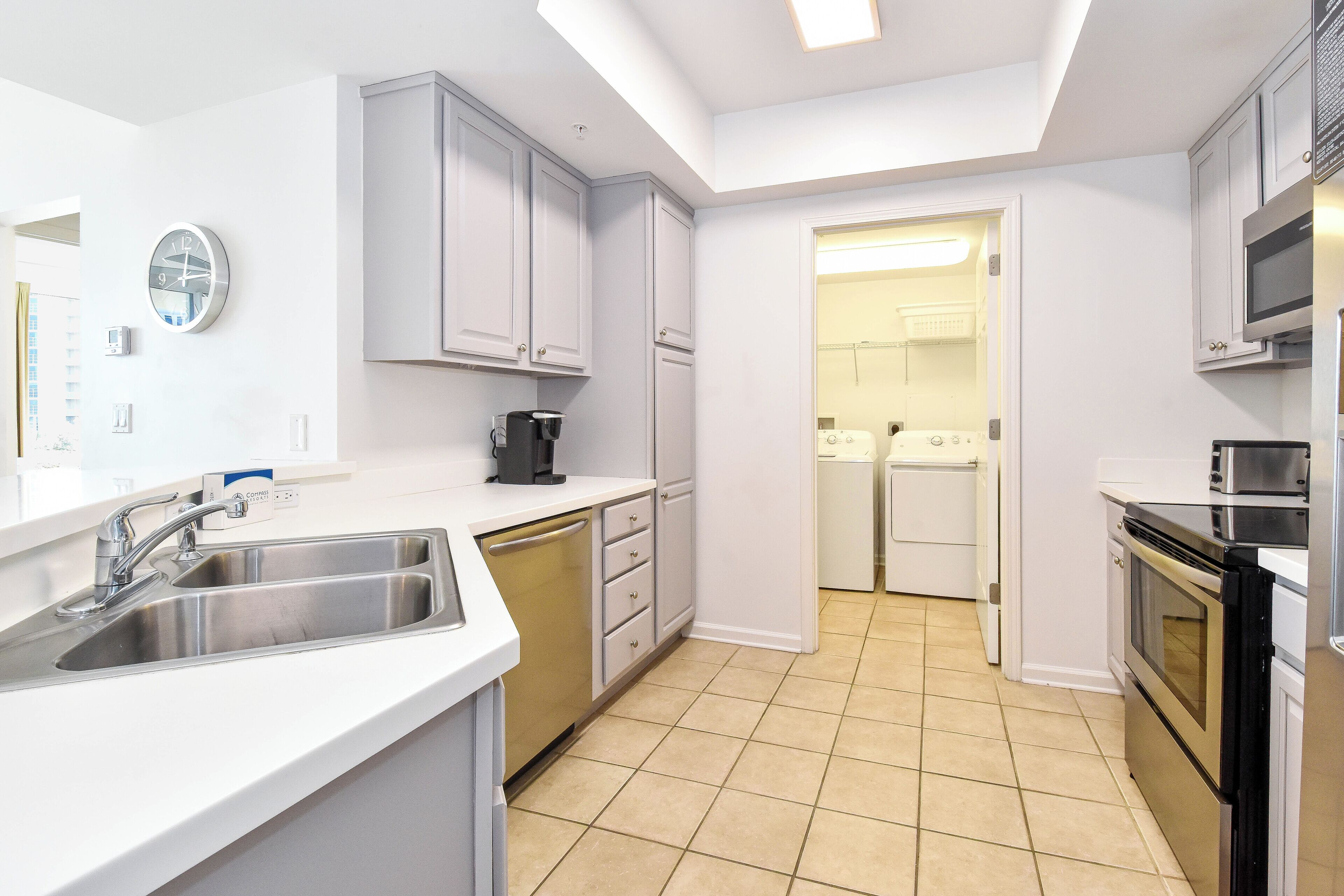 A modern kitchen with white cabinets, a stainless steel sink, a coffee maker, and a microwave.