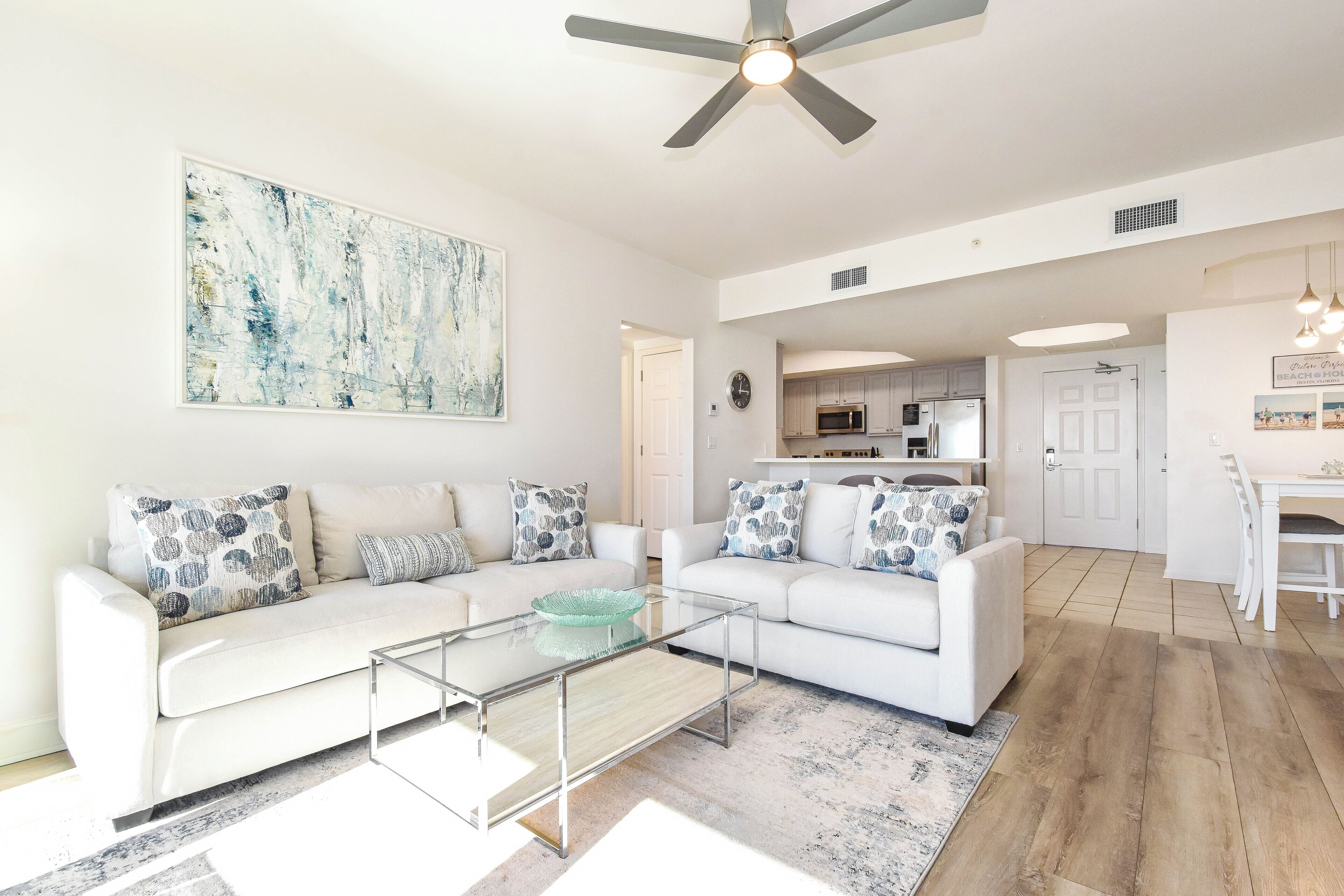 A modern living room with a white sofa, glass coffee table, and abstract art on the wall.