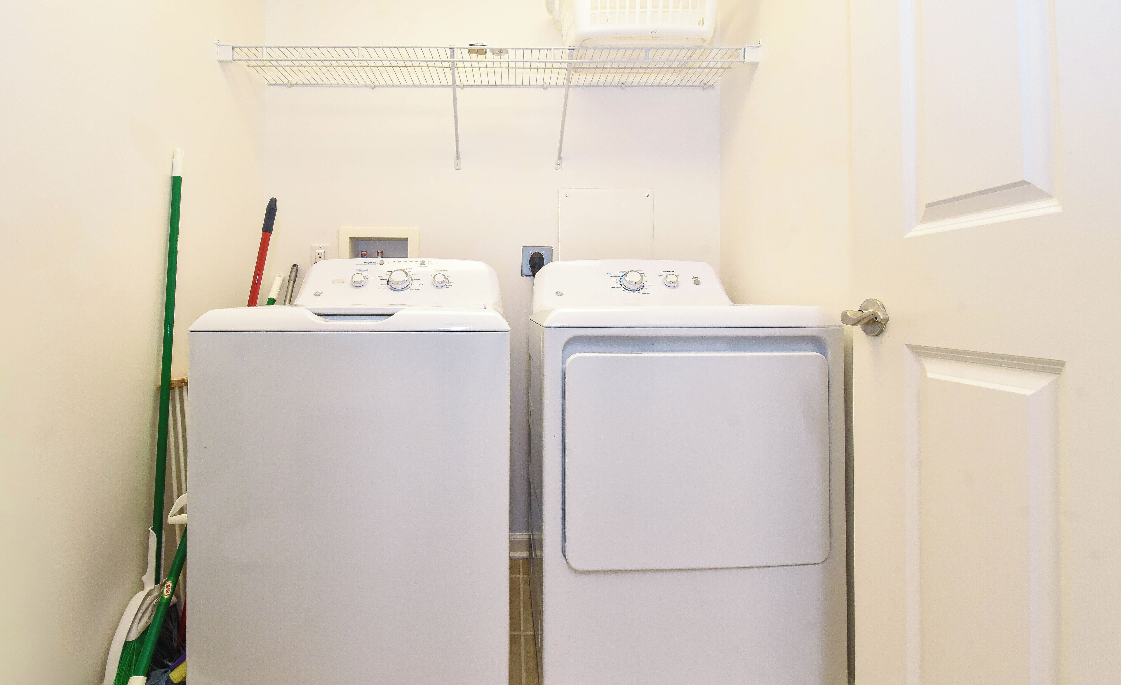 A laundry room with two white front-loading washing machines and a drying rack above them.