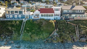 A coastal residential area with houses, a wooden staircase leading to a beach, and a rocky shoreline.