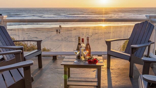 A beachside patio with Adirondack chairs and a table set with wine bottles and glasses.