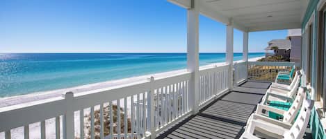 A covered porch with a view of a beach and ocean.