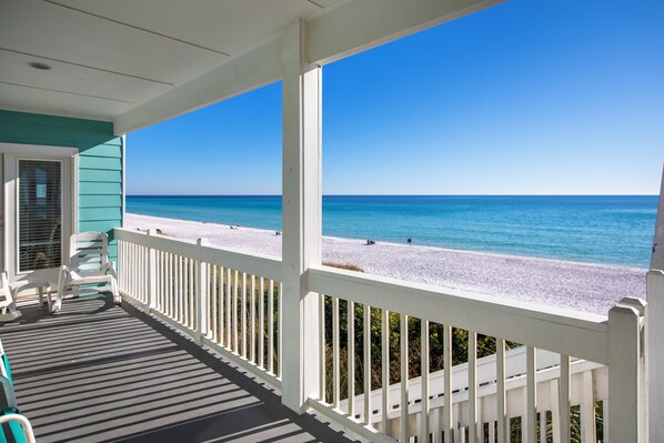 A covered porch with a view of a beach.