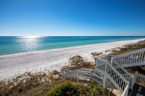 A beach with a staircase leading down to the sand, clear blue water, and a clear sky.