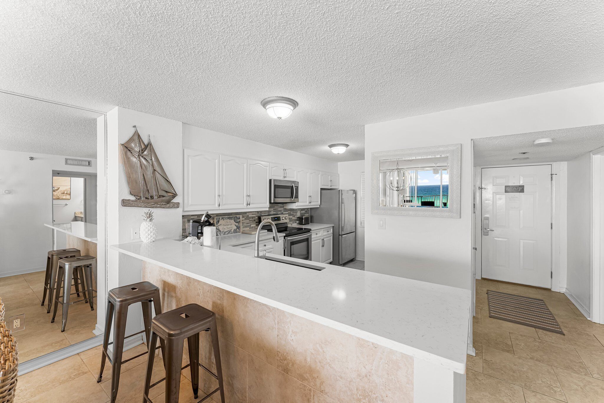 A modern kitchen with white cabinetry, stainless steel appliances, and a large island with stools.