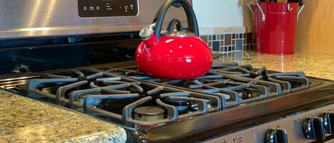 A kitchen with a stainless steel stove, a red kettle, and a red bucket with utensils.