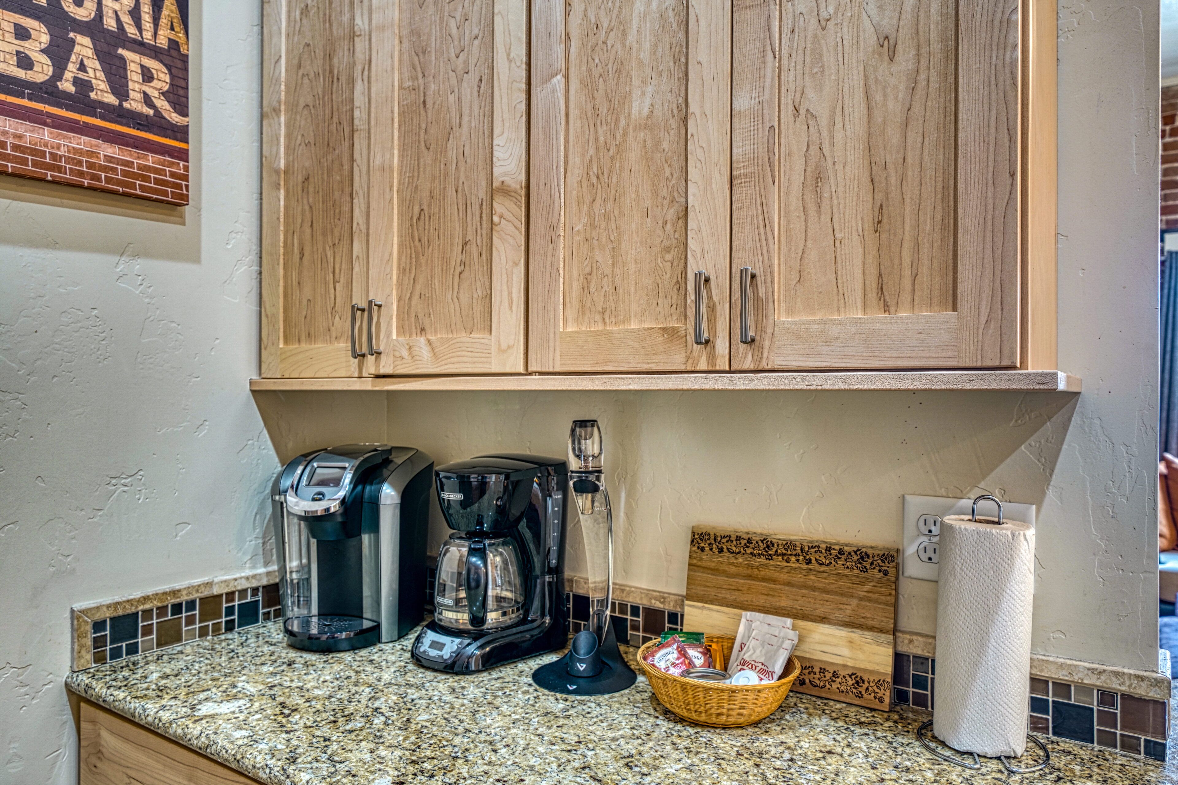A kitchen with wooden cabinets, a coffee maker, a basket, and a paper towel holder.