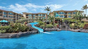 A hotel pool with a water slide, surrounded by lush greenery and palm trees.