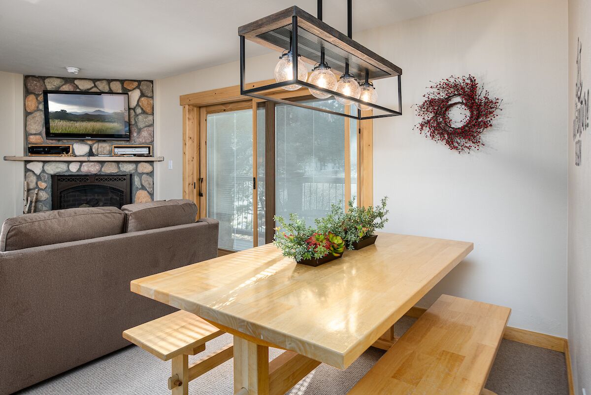 Un salon moderne avec une cheminée en pierre, une table à manger en bois avec des bancs, un canapé et un téléviseur fixé à un mur en pierre.
