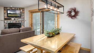 Un salon moderne avec une cheminée en pierre, une table à manger en bois avec des bancs, un canapé et un téléviseur fixé à un mur en pierre.