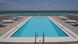 Ein rechteckiger Pool mit einem Sprungverbotsschild, umgeben von Liegestühlen und einem Metallgeländer, mit Blick auf den Ozean.