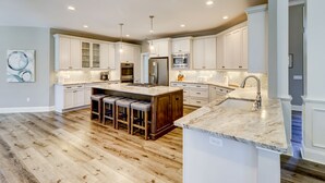 A spacious kitchen with white cabinets, a central island with stools, stainless steel appliances, and a marble countertop. - 37 St. George - 5 minute walk to the beach! (Hilton Head Island)