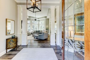 A spacious hallway with a large mirror, a decorative cabinet, and a modern chandelier.