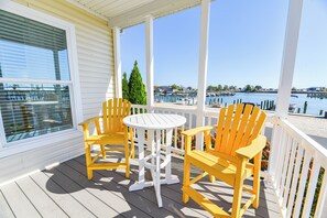 Een overdekt terras met gele Adirondack-stoelen en een witte tafel, met uitzicht op een jachthaven vol boten en een helderblauwe lucht.
