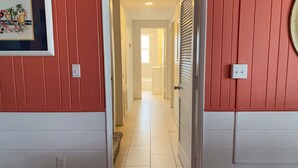 Een gang met een betegelde vloer, een lijst met een afbeelding aan de muur en een deur die naar een andere kamer leidt.