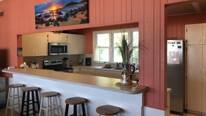 Een keuken met een bar, witte kastjes, een roestvrijstalen koelkast en een schilderij van een zonsondergang boven de oceaan.