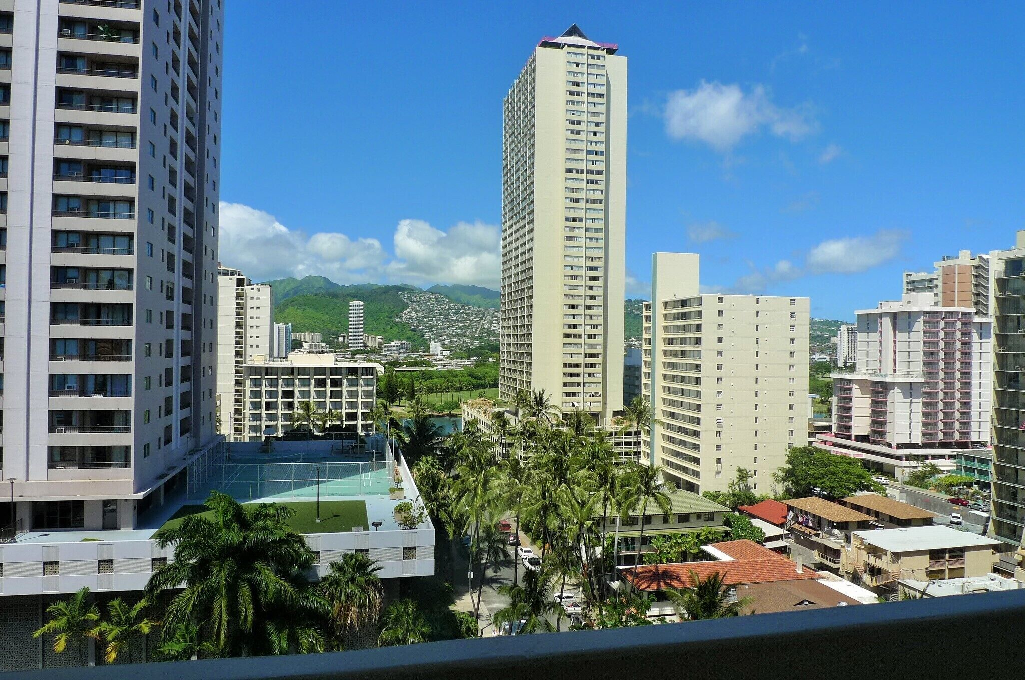 A high-rise hotel with multiple floors, a rooftop pool, and a view of a cityscape with mountains in the background.