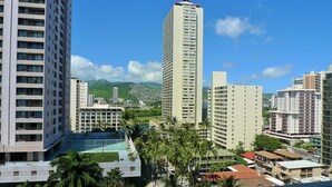 A high-rise hotel with multiple floors, a rooftop pool, and a view of a cityscape with mountains in the background.