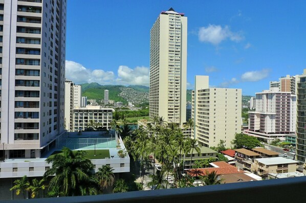 A high-rise hotel with multiple floors, a rooftop pool, and a view of a cityscape with mountains in the background.