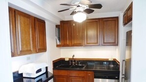A kitchen with wooden cabinets, a black countertop, a stainless steel dishwasher, and a ceiling fan.