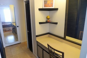 A corner kitchenette with a small table and chair, a shelf with a vase of flowers, and a framed picture above the shelf.