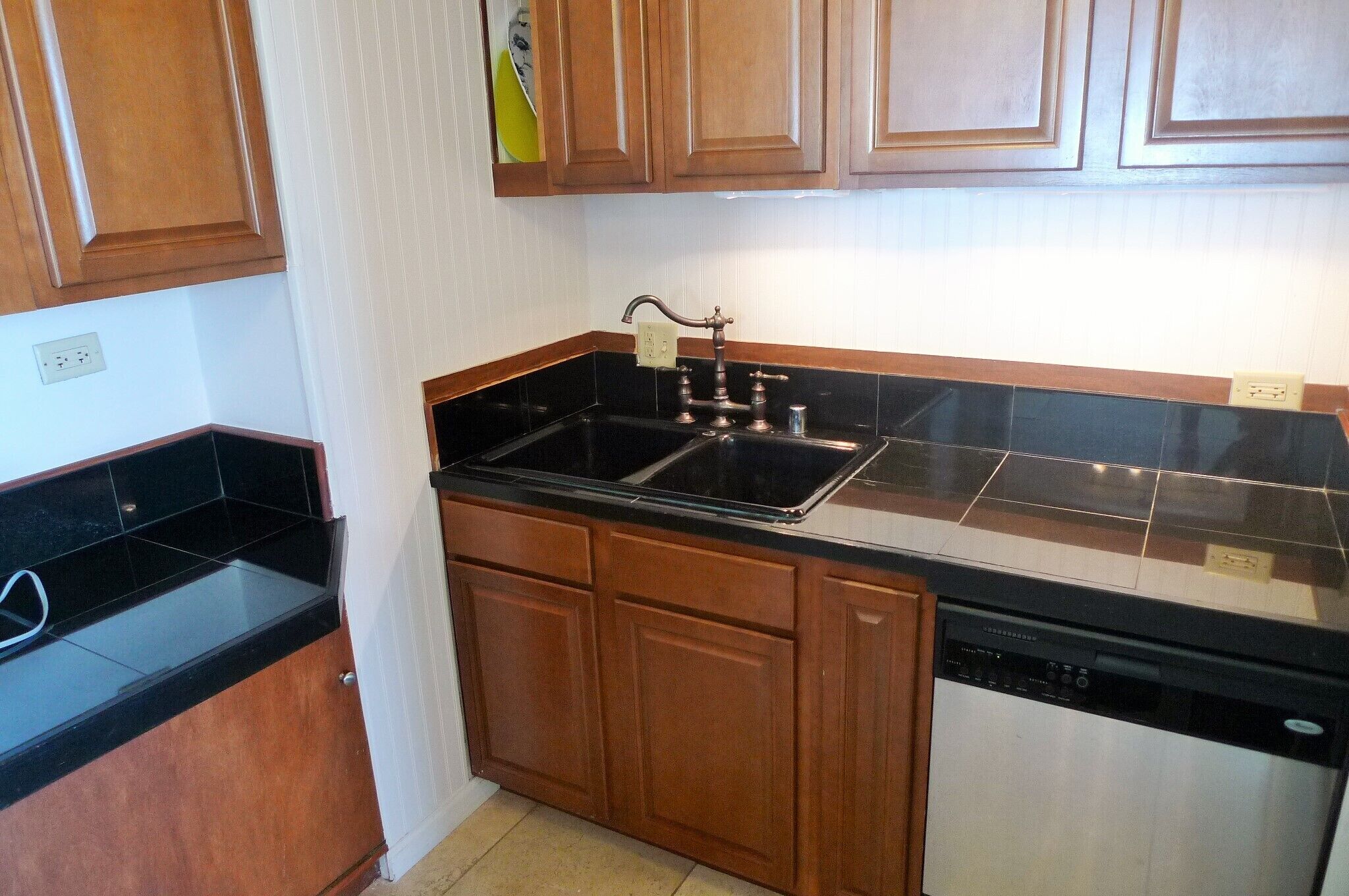 A kitchen with wooden cabinets, a black countertop, and a dishwasher.