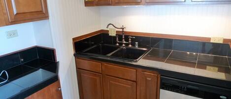 A kitchen with wooden cabinets, a black countertop, and a dishwasher.