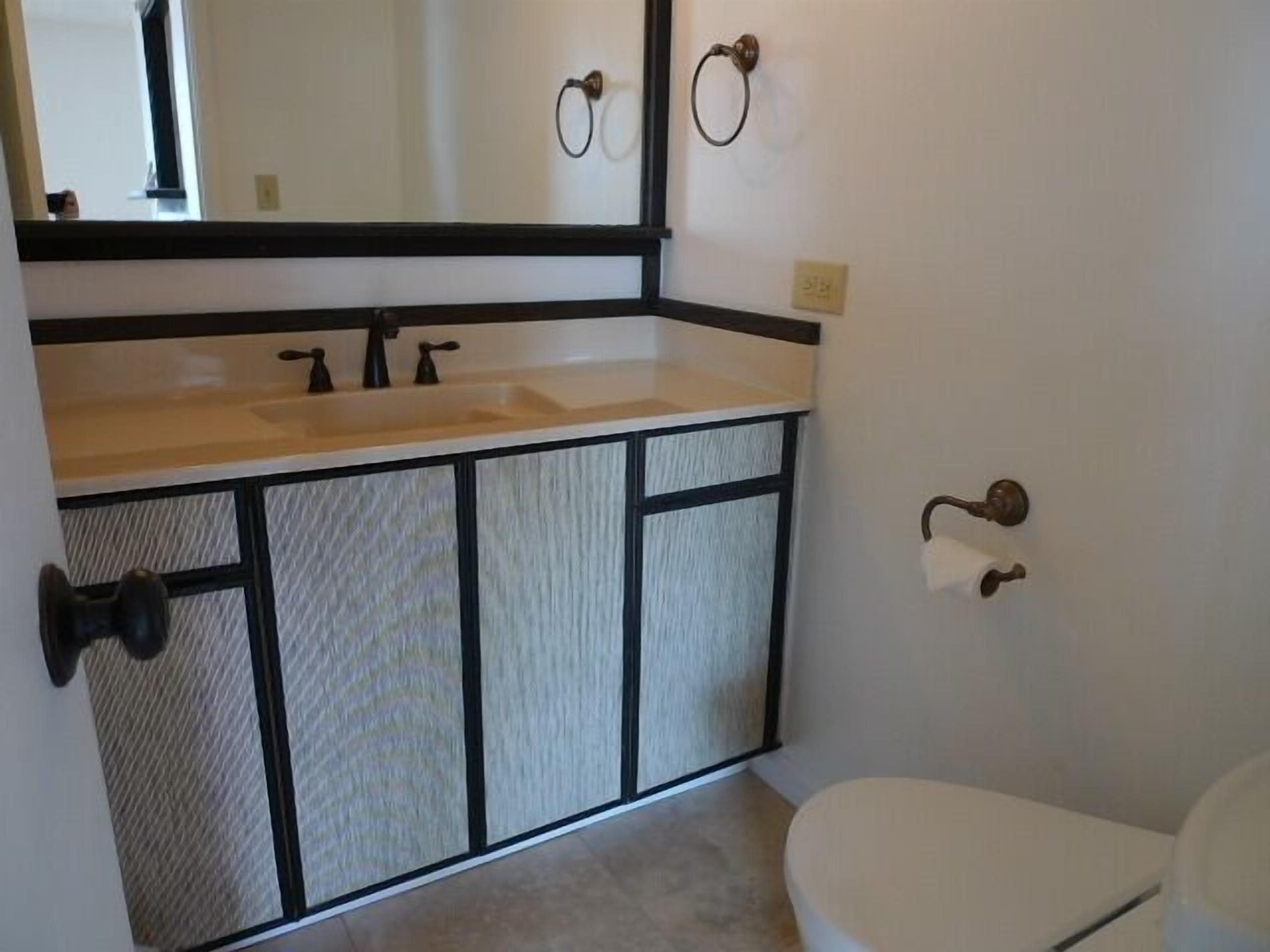 Bany amb un lavabo blanc, un armari negre i un vàter.