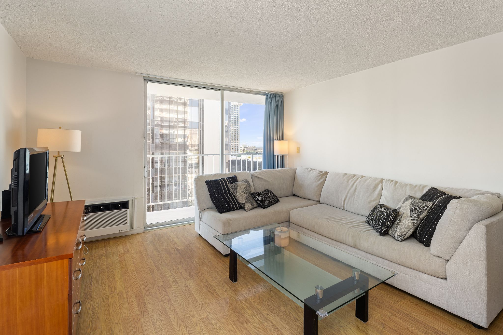 A modern living room with a sofa, a glass coffee table, a TV, and a lamp.