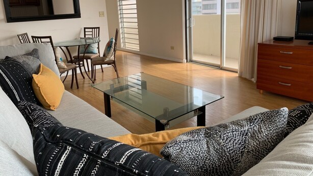 A modern living room with a glass coffee table, a sofa, and a dining area with chairs.