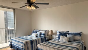 A bedroom with two beds, a ceiling fan, and a window with a view of buildings.