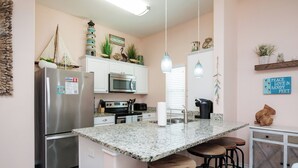 A kitchen with a stainless steel refrigerator, a microwave, and a sink. There are bar stools and a countertop. - Pet-Friendly Beach Escape | Pool Access & Walk to Beach (Corpus Christi)