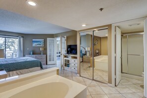 Un dormitorio con una cama grande, televisión, escritorio y baño con bañera.