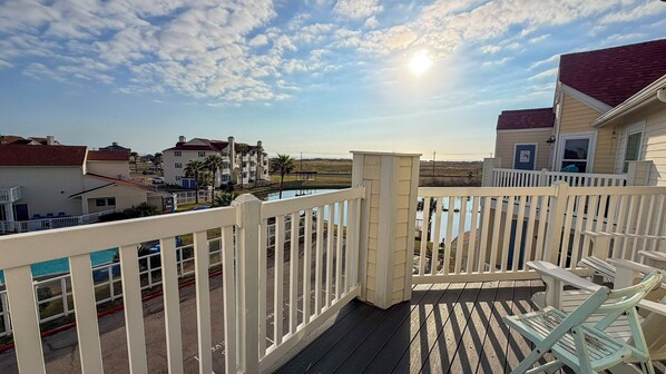 Une terrasse en bois avec une balustrade blanche, donnant sur une piscine et offrant une vue sur les bâtiments voisins.