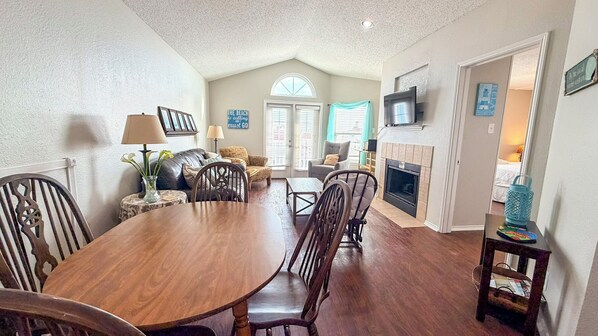 A dining area with a wooden table and chairs, a fireplace, and a television mounted above it.