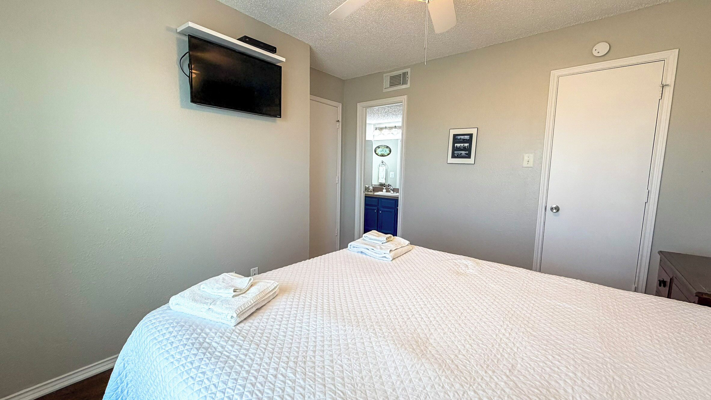 Een slaapkamer met een bed, een aan de muur bevestigde televisie, een deur en een raam.