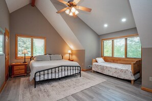 A bedroom with a sloped ceiling, a bed, a bench, and two windows with blinds. - Tranquil Lakefront w/ Twin Hot Tubs & Dock (Oakland)