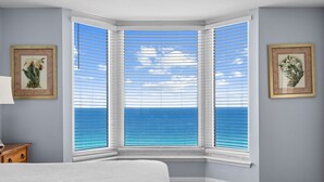 A bedroom with a bay window, a bed, a nightstand, and two framed pictures on the wall. - BEACHFRONT UNIT!! COMFORTABLY SLEEPS 8! UPDATED JUNE 2026!! (Panama City Beach)