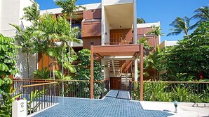 A resort with a covered outdoor area, palm trees, and a staircase leading to a building.