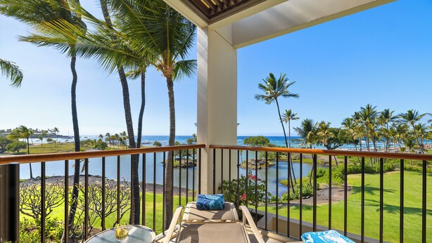 A balcony with a view of the ocean, palm trees, and a grassy area.